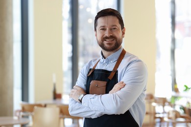 Portrait of smiling business owner with crossed arms in his cafe. Space for text