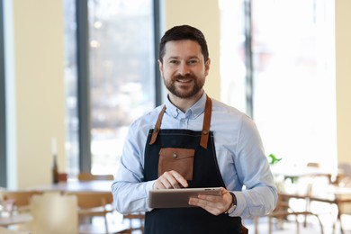 Photo of Portrait of smiling business owner with tablet in his cafe