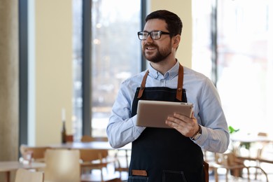 Smiling business owner with tablet in his cafe. Space for text