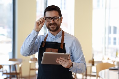 Photo of Portrait of smiling business owner with tablet in his cafe