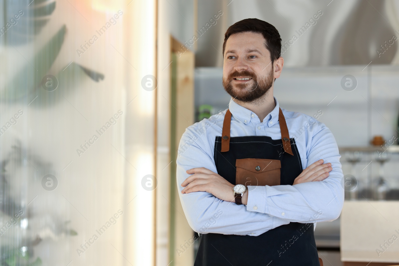 Photo of Smiling business owner with crossed arms in his cafe. Space for text