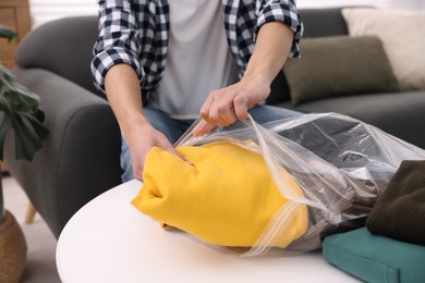 Photo of Man packing clothes into vacuum bag at table indoors, closeup