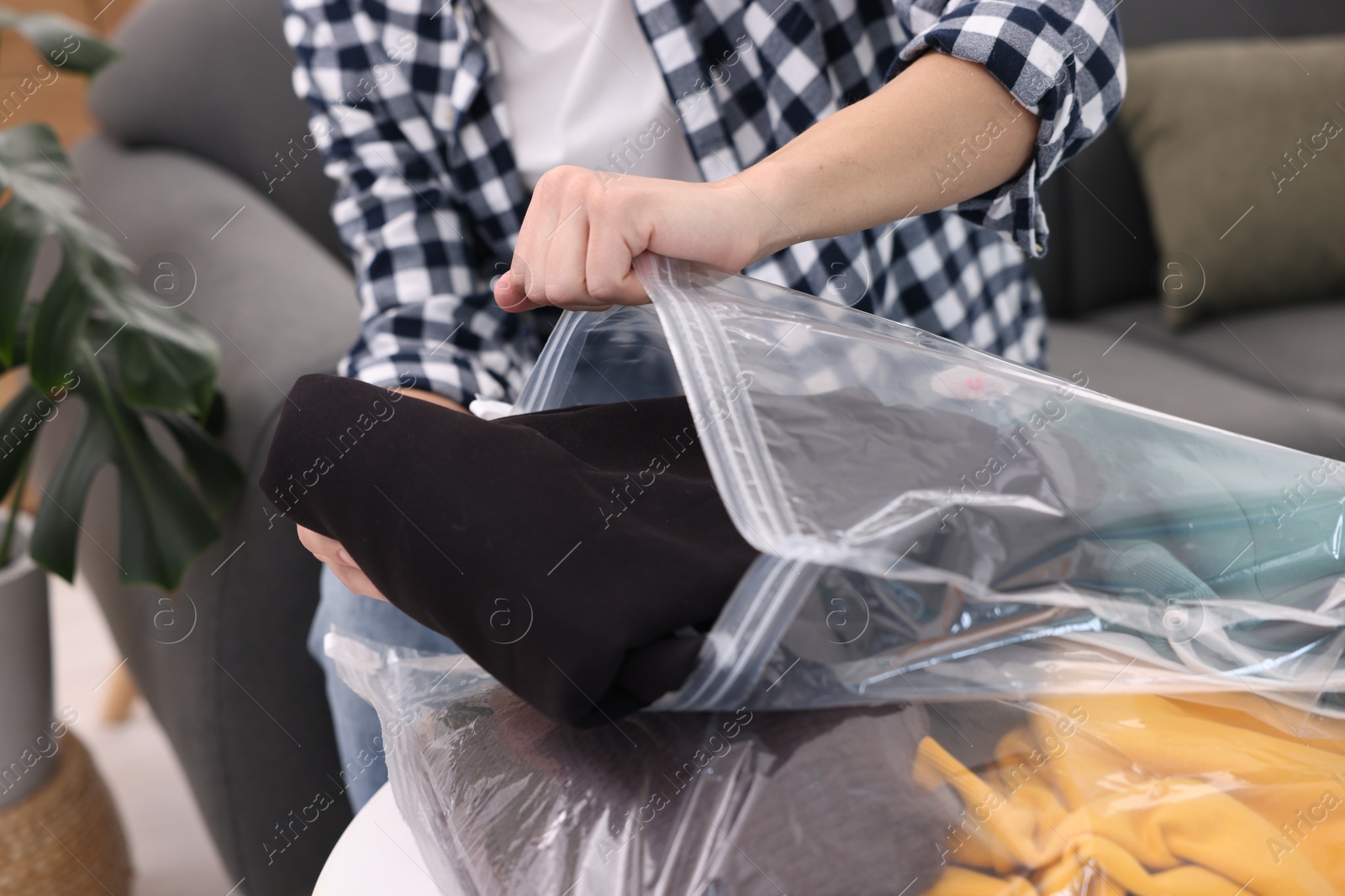 Photo of Man packing clothes into vacuum bag at table indoors, closeup