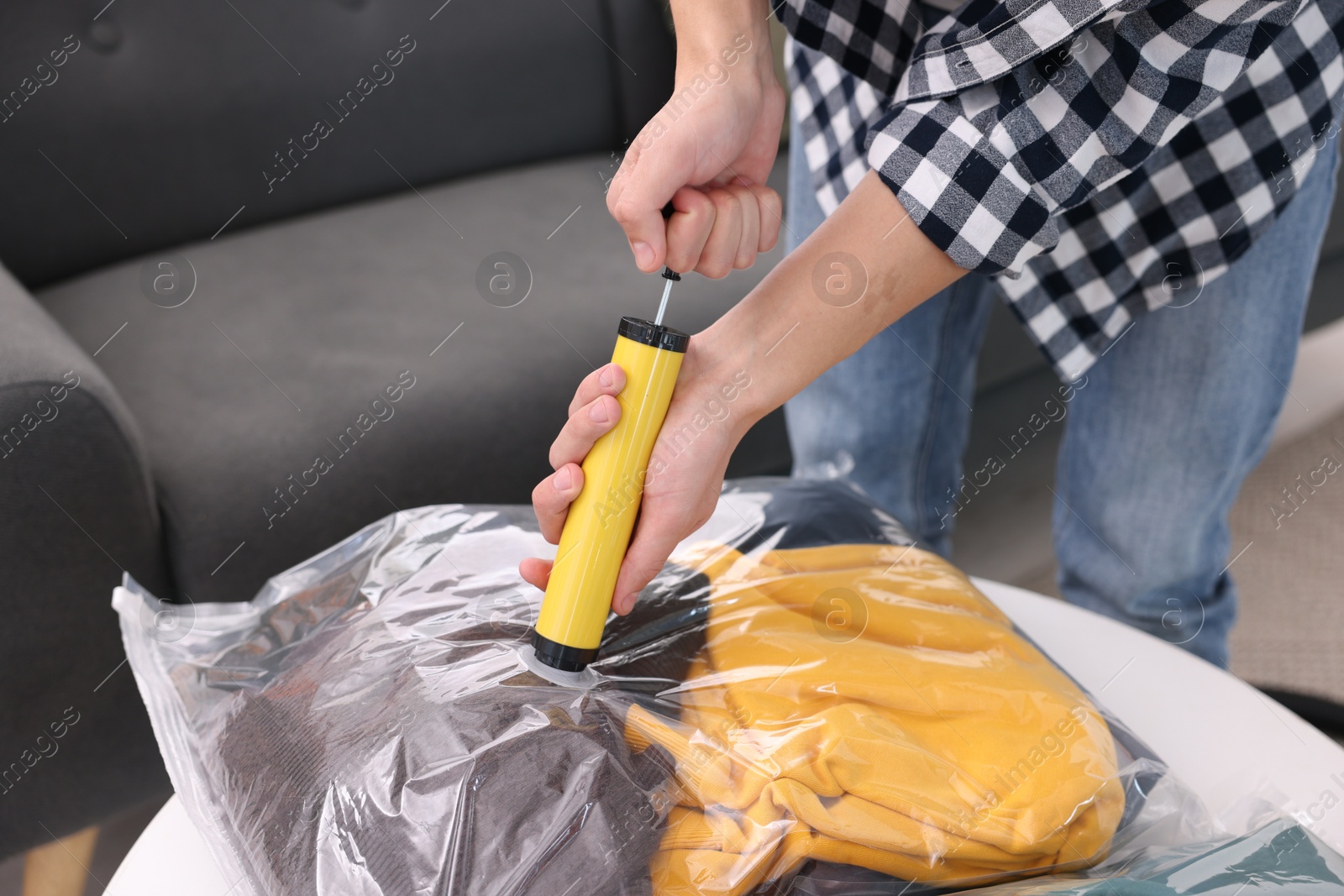 Photo of Man sealing vacuum bag with clothes at table indoors, closeup