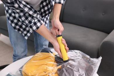 Photo of Man sealing vacuum bag with clothes at table indoors, closeup