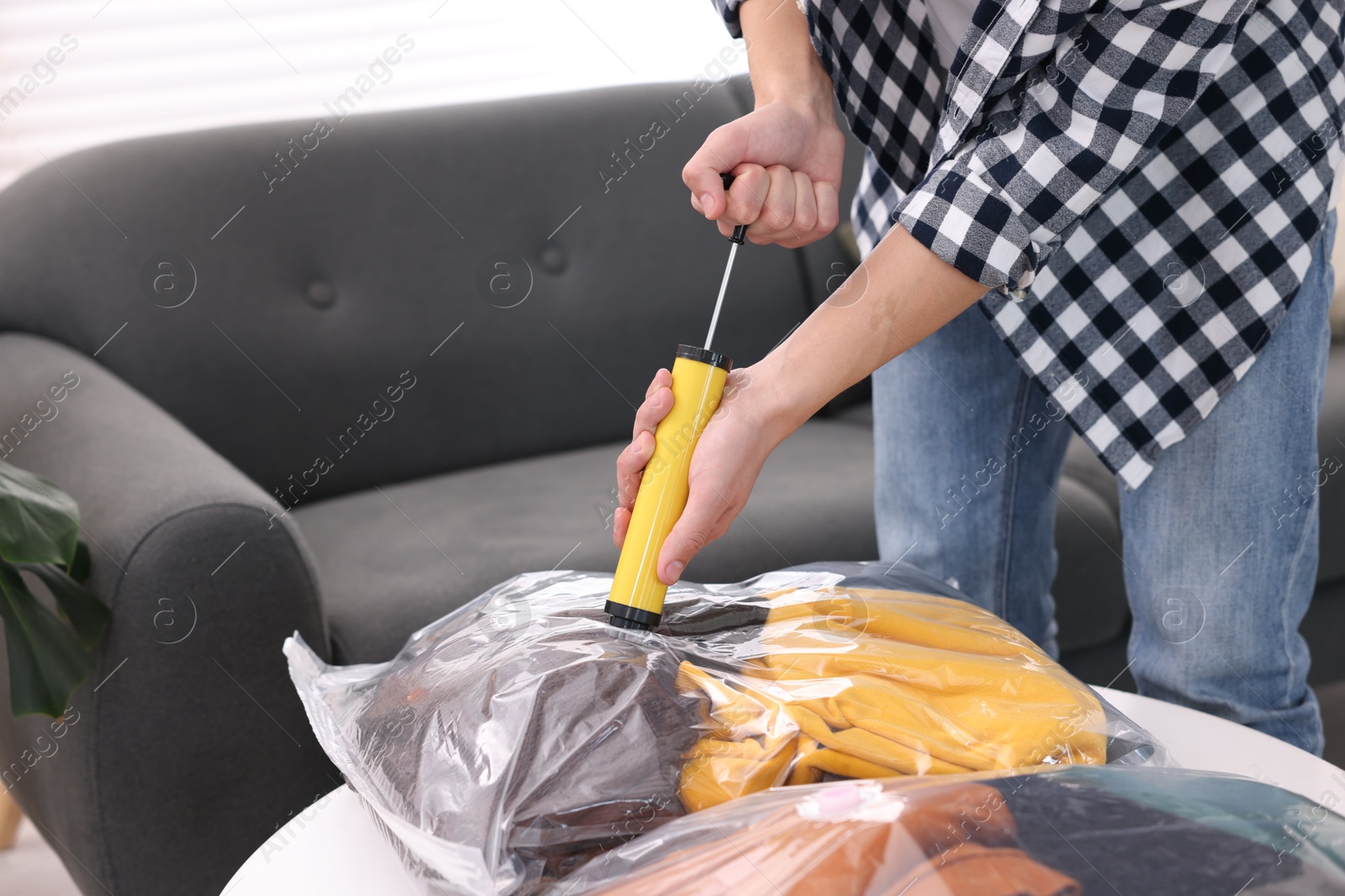 Photo of Man sealing vacuum bag with clothes at table indoors, closeup