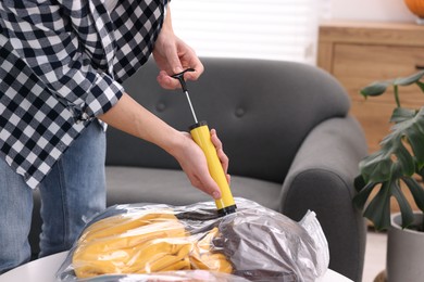 Photo of Man sealing vacuum bag with clothes at table indoors, closeup