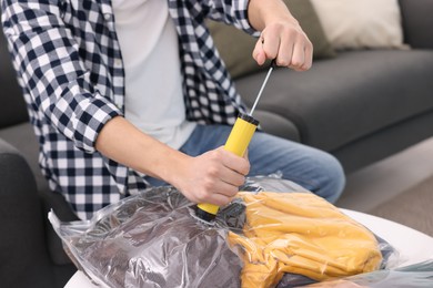 Photo of Man sealing vacuum bag with clothes at table indoors, closeup