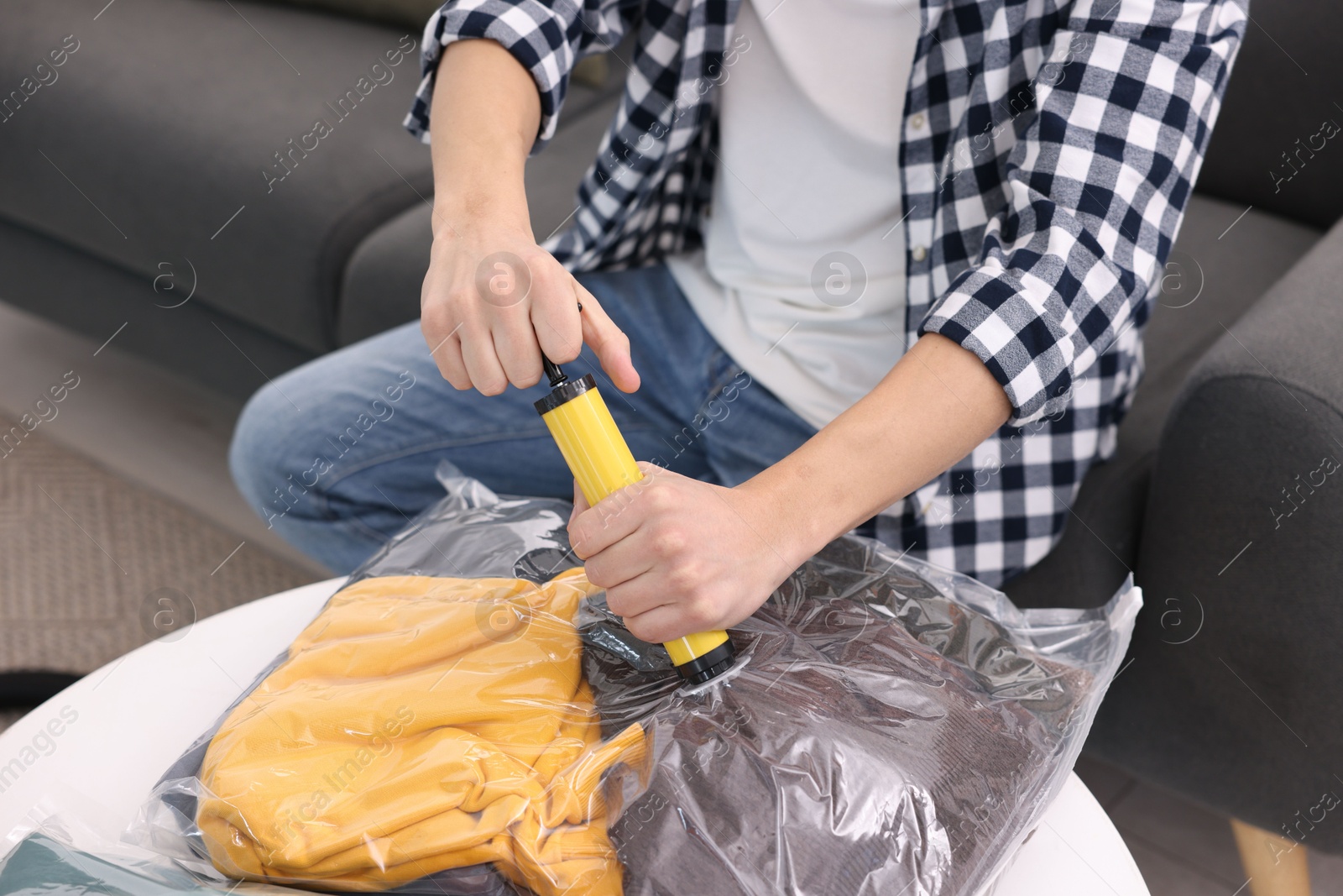 Photo of Man sealing vacuum bag with clothes at table indoors, closeup