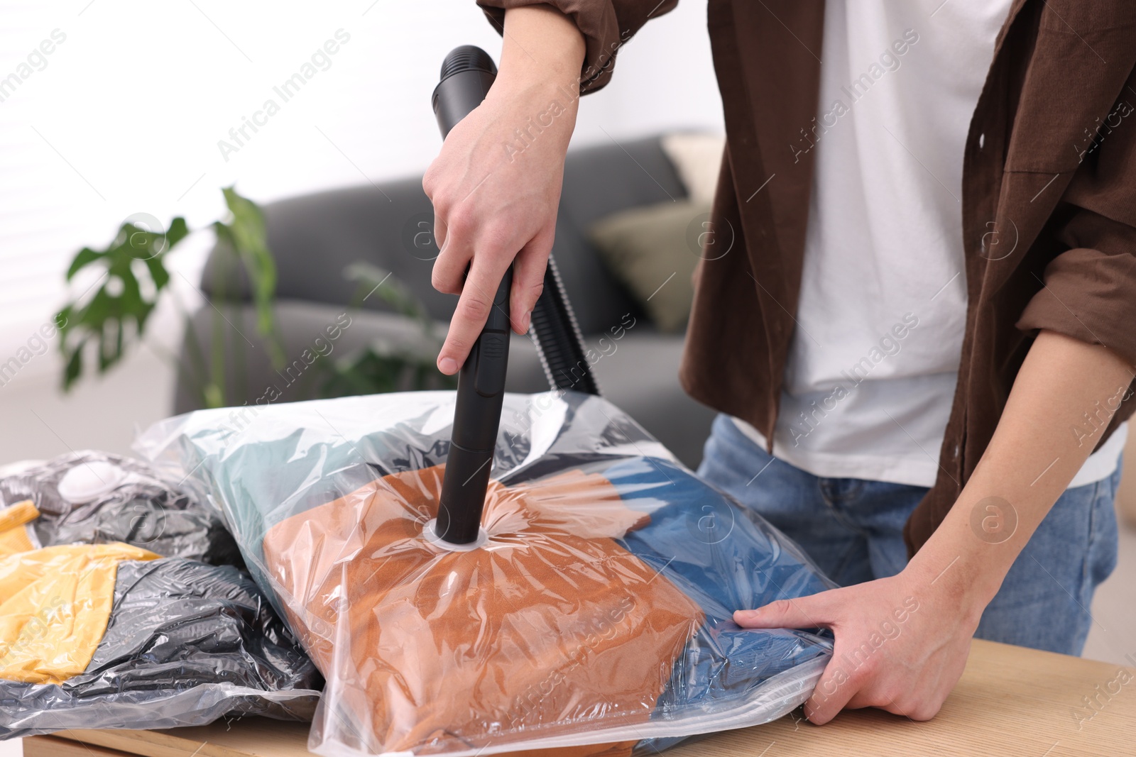 Photo of Man sealing vacuum bag with clothes at table indoors, closeup