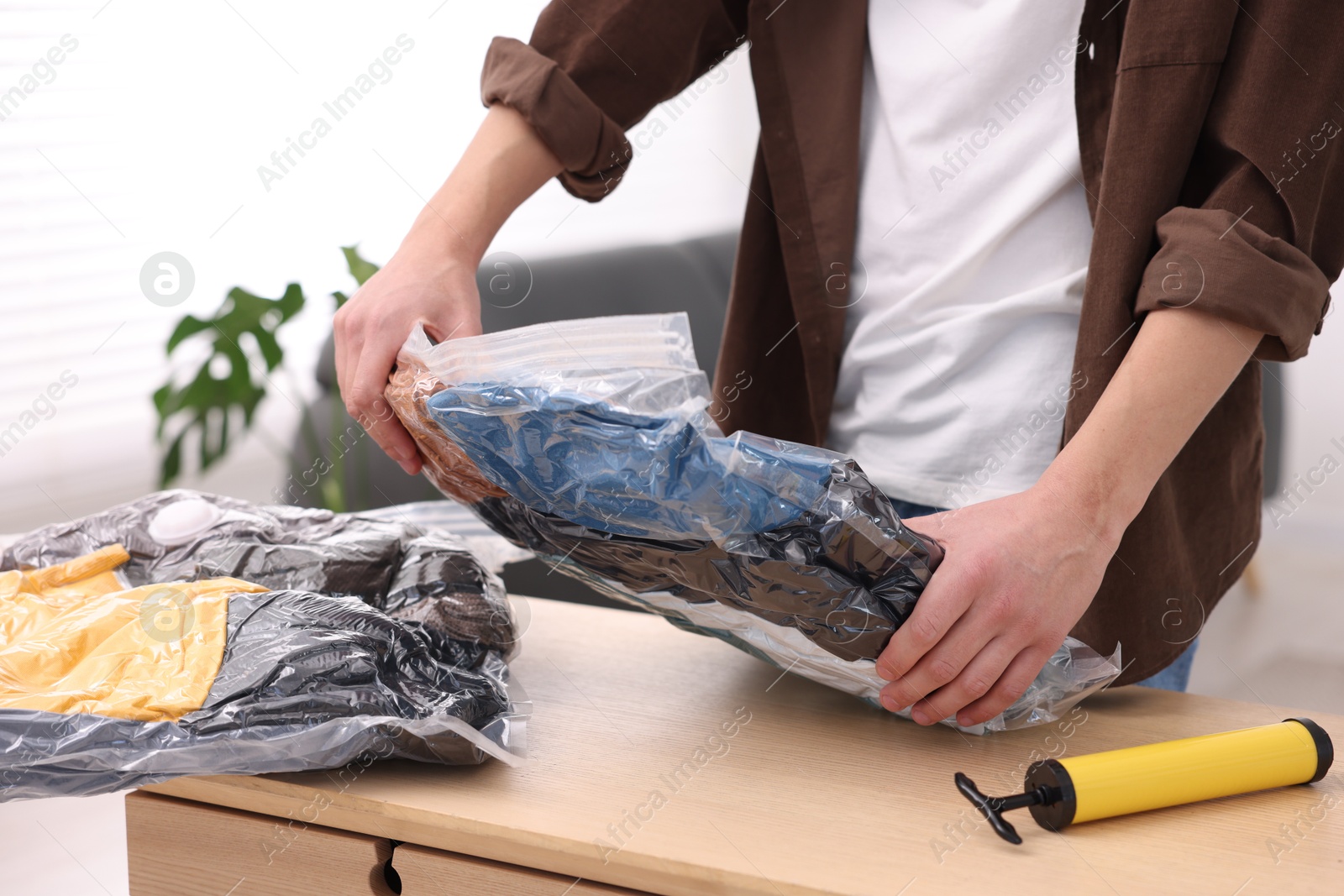 Photo of Man packing clothes into vacuum bag at table indoors, closeup