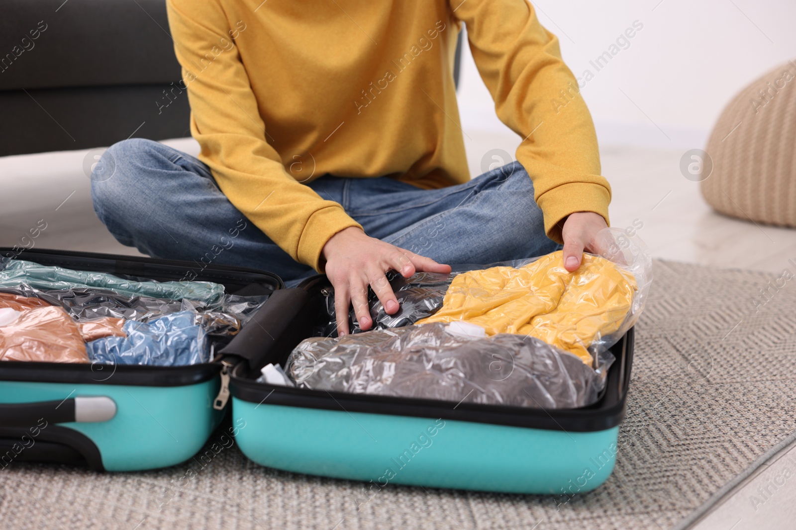 Photo of Man packing clothes into vacuum bag on floor indoors, closeup