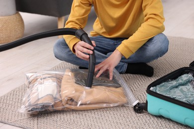 Photo of Man sealing vacuum bag with clothes on floor indoors, closeup