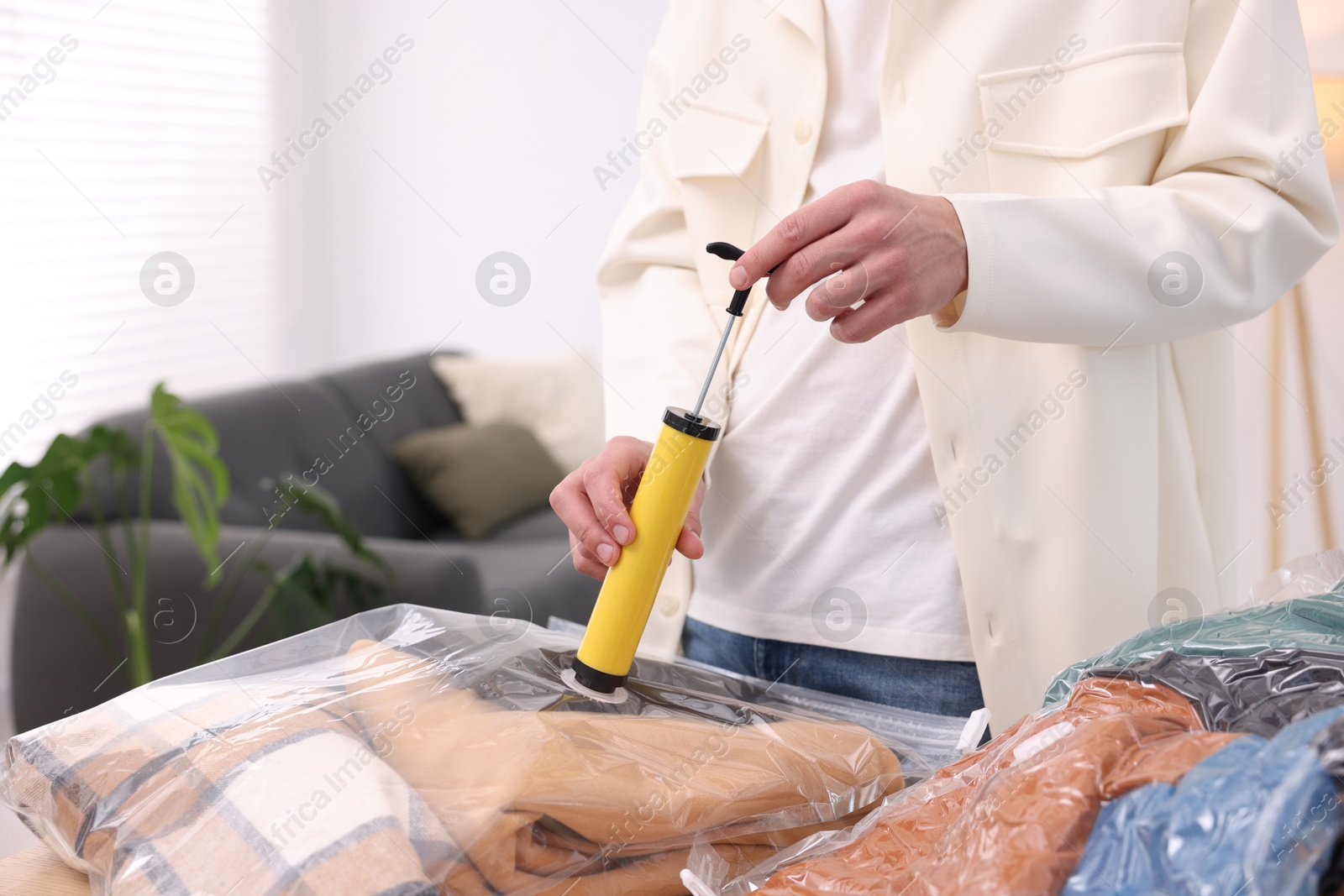 Photo of Man packing clothes into vacuum bag at table indoors, closeup