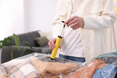 Photo of Man packing clothes into vacuum bag at table indoors, closeup