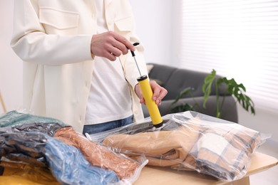 Photo of Man packing clothes into vacuum bag at table indoors, closeup