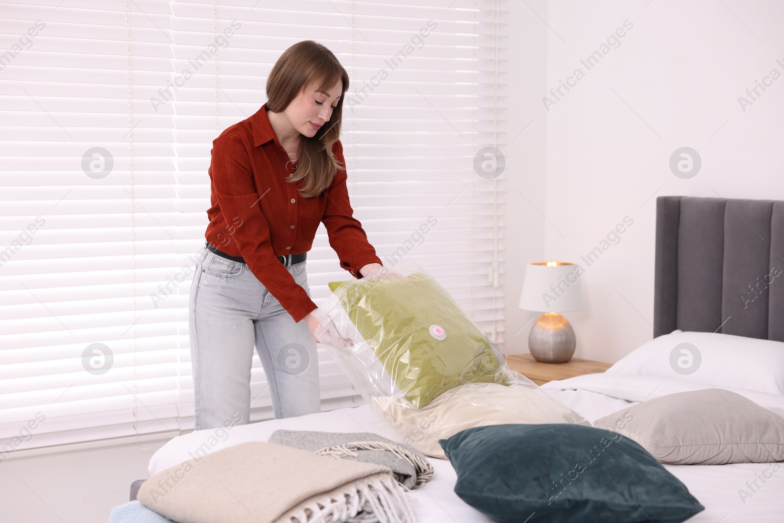 Photo of Woman packing pillow into vacuum bag at home