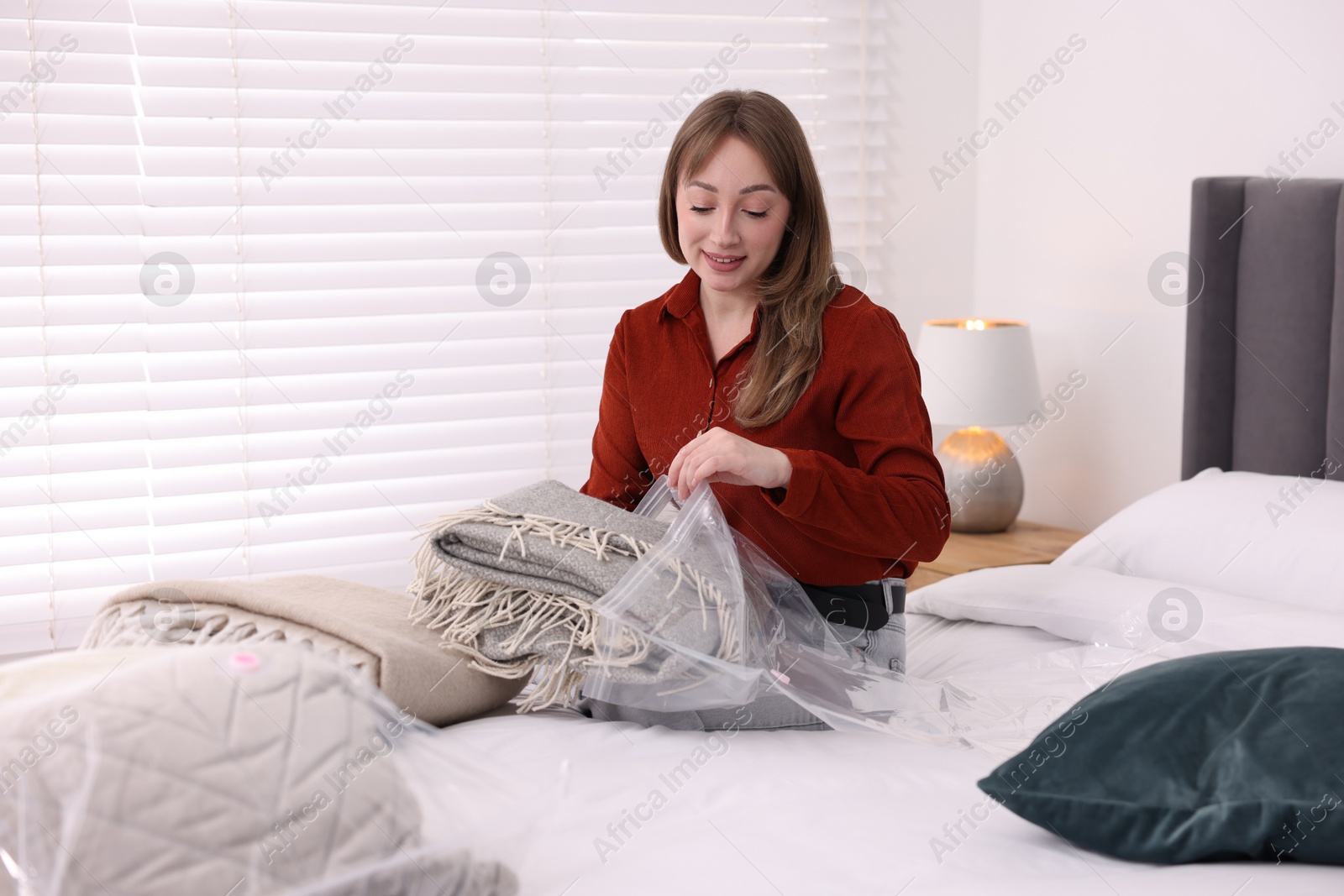 Photo of Woman packing blanket into vacuum bag on bed at home