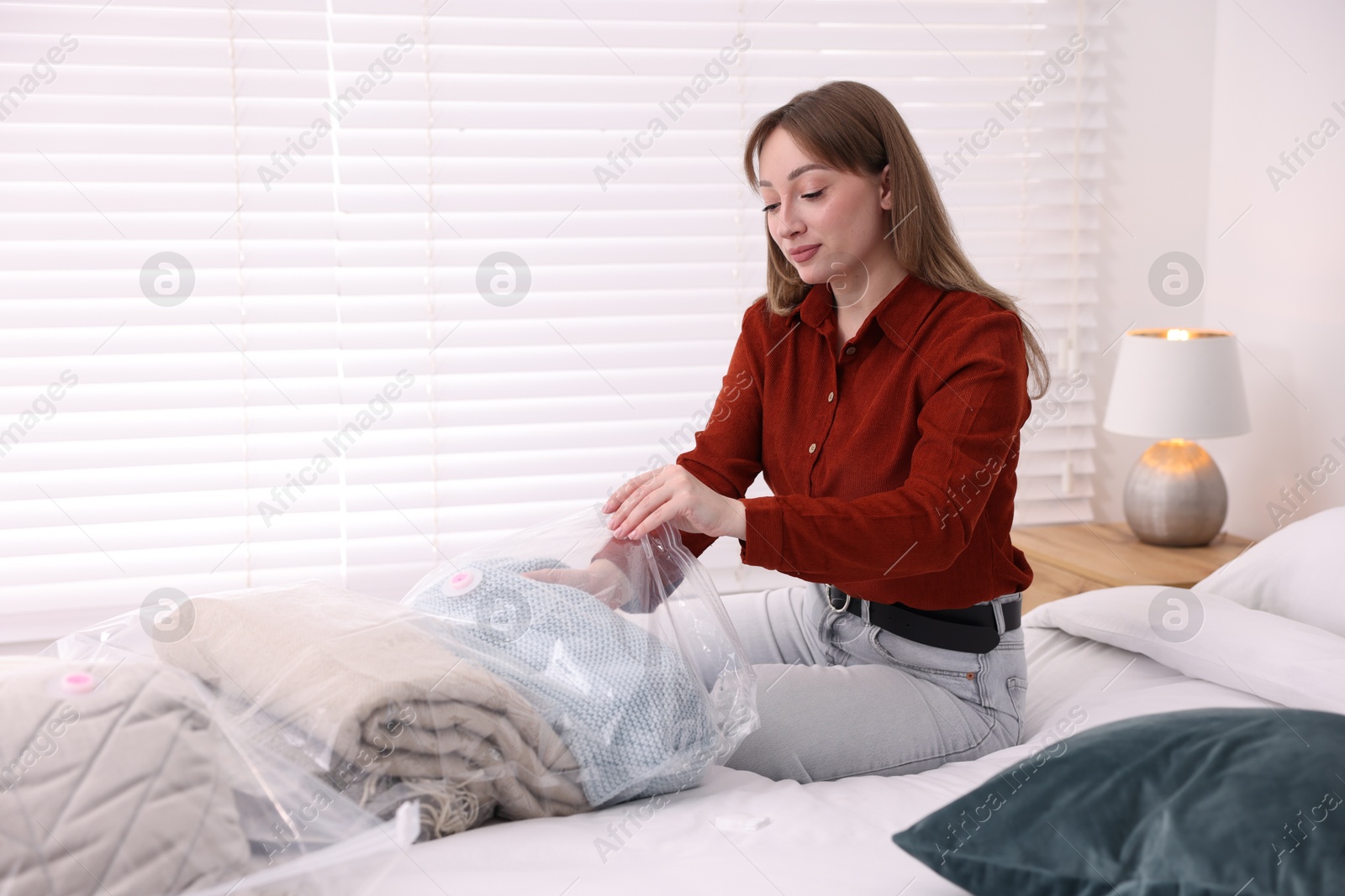 Photo of Woman packing blanket into vacuum bag on bed at home