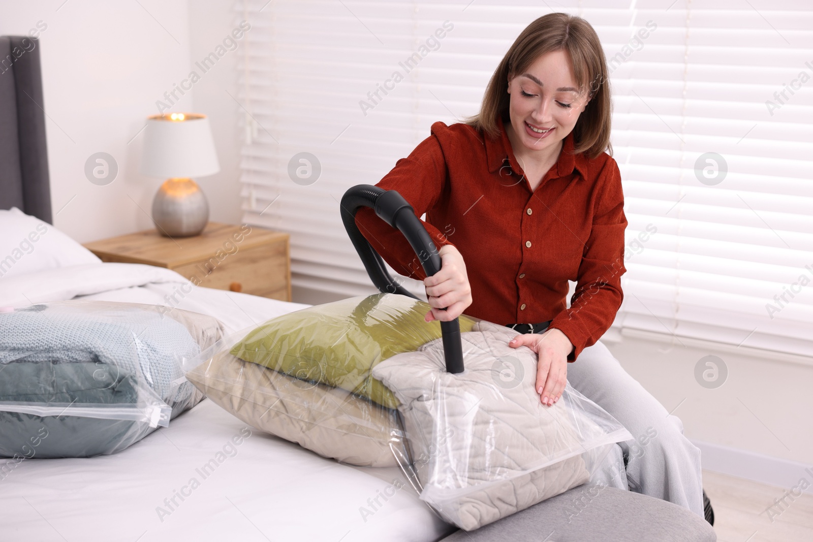 Photo of Woman sealing vacuum bag with pillows on bed at home