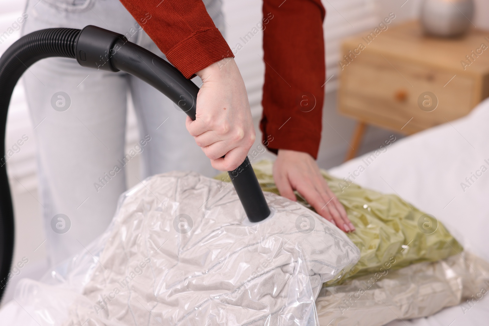 Photo of Woman sealing vacuum bag with pillows at home, closeup