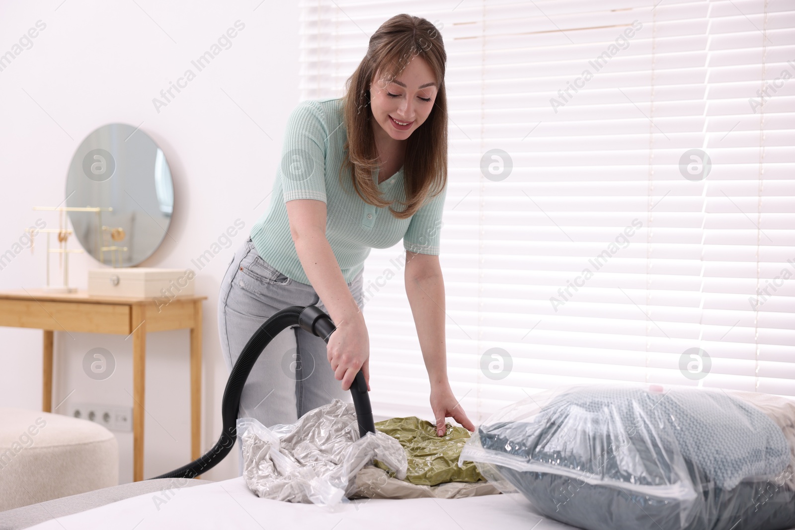 Photo of Woman sealing vacuum bag with pillows at home