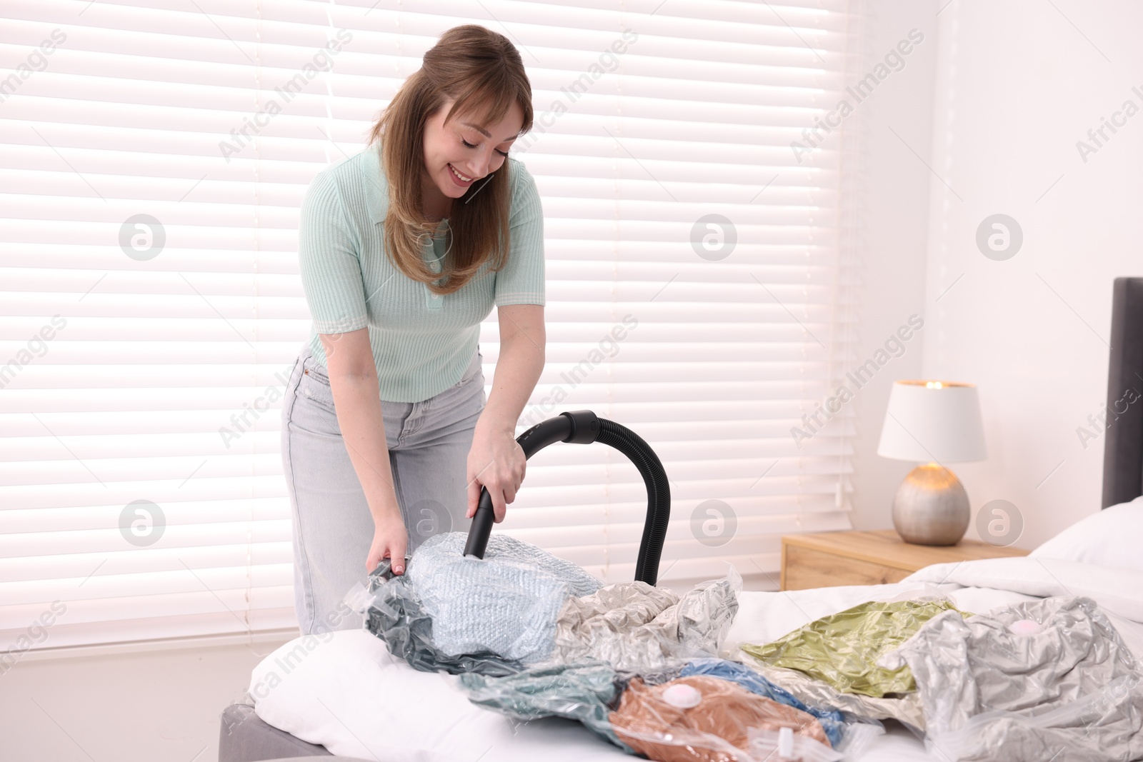 Photo of Woman sealing vacuum bag with blankets at home