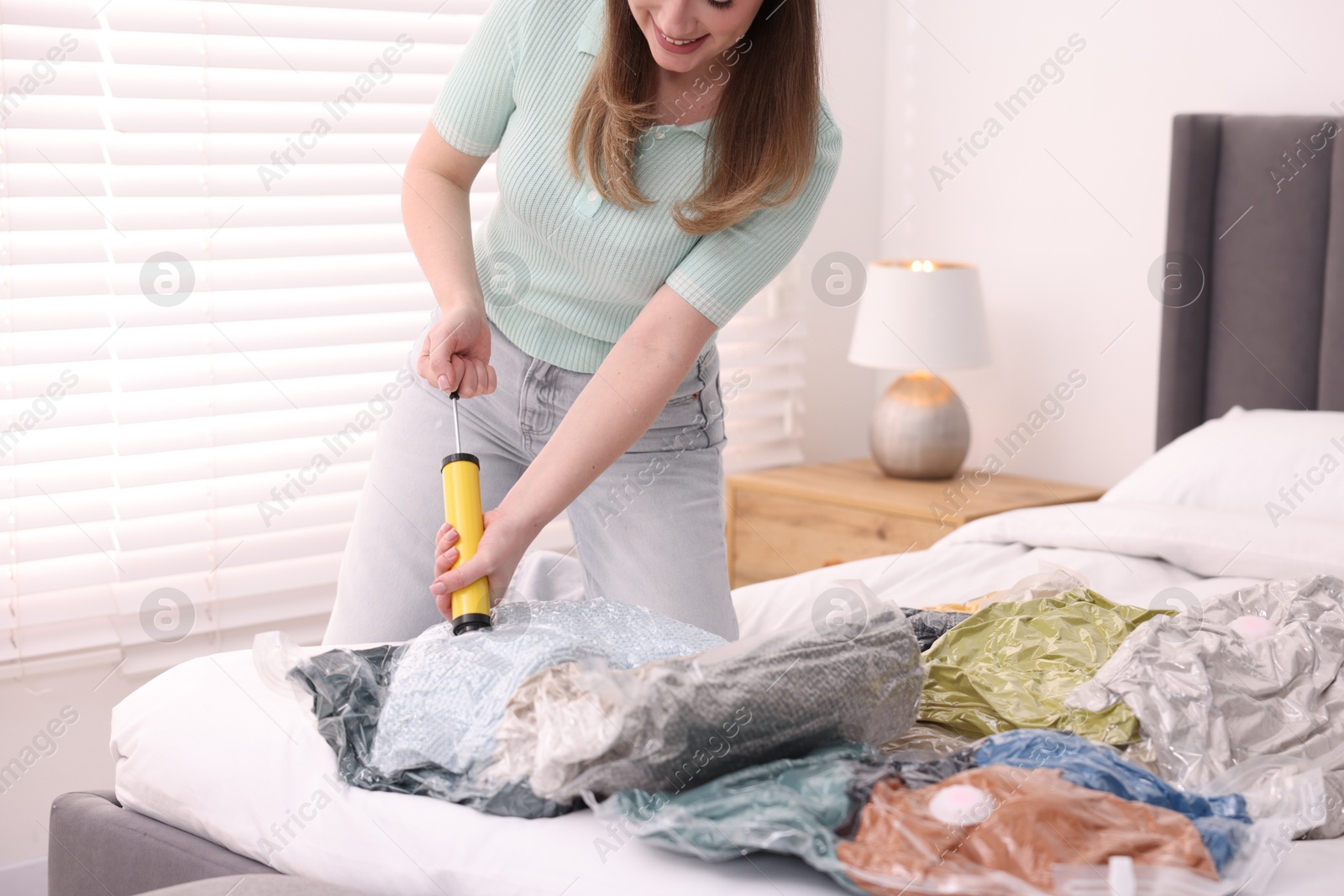 Photo of Woman sealing vacuum bag with blankets at home, closeup