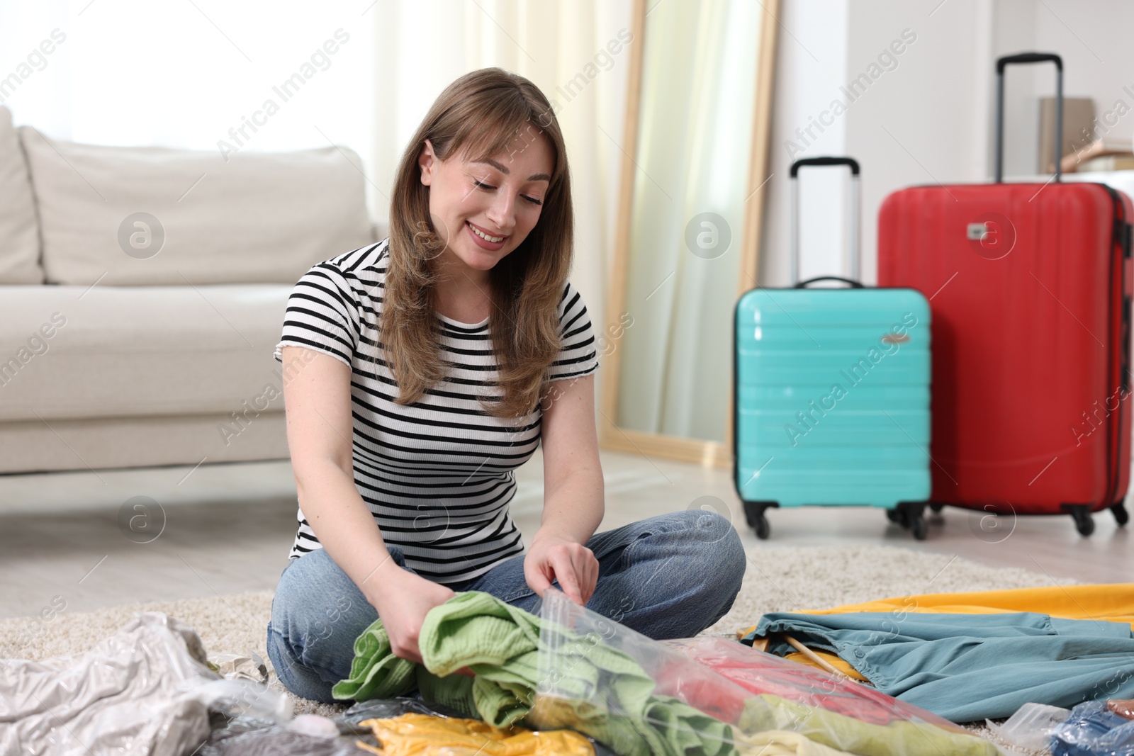 Photo of Woman packing clothes into vacuum bag on floor at home