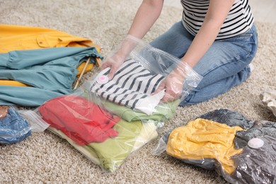 Photo of Woman packing clothes into vacuum bag on floor at home, closeup