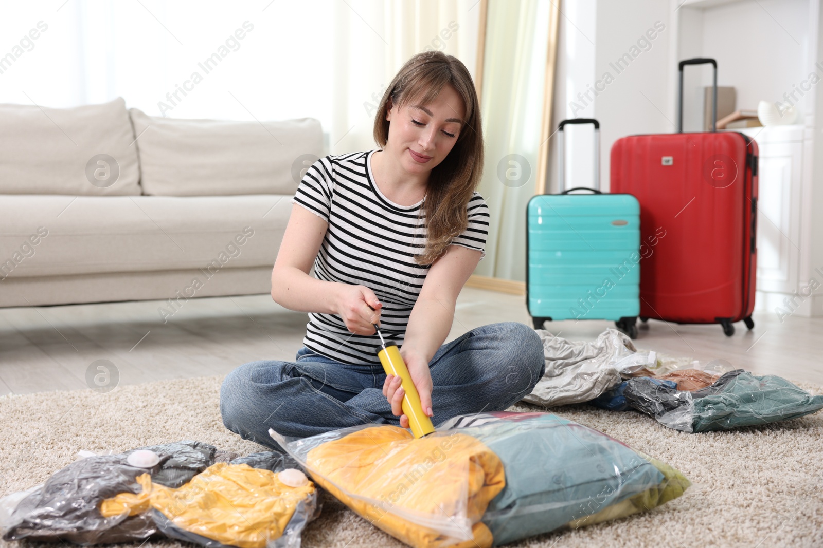 Photo of Woman sealing vacuum bag with clothes on floor at home