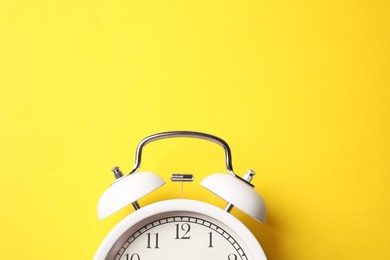 Photo of White alarm clock on yellow background, top view. Space for text