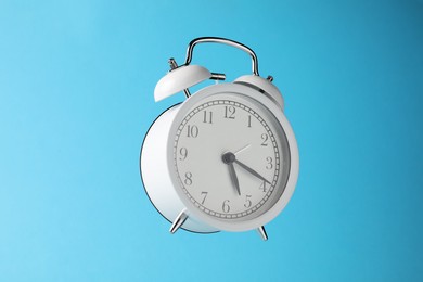 Photo of White alarm clock in air on light blue background