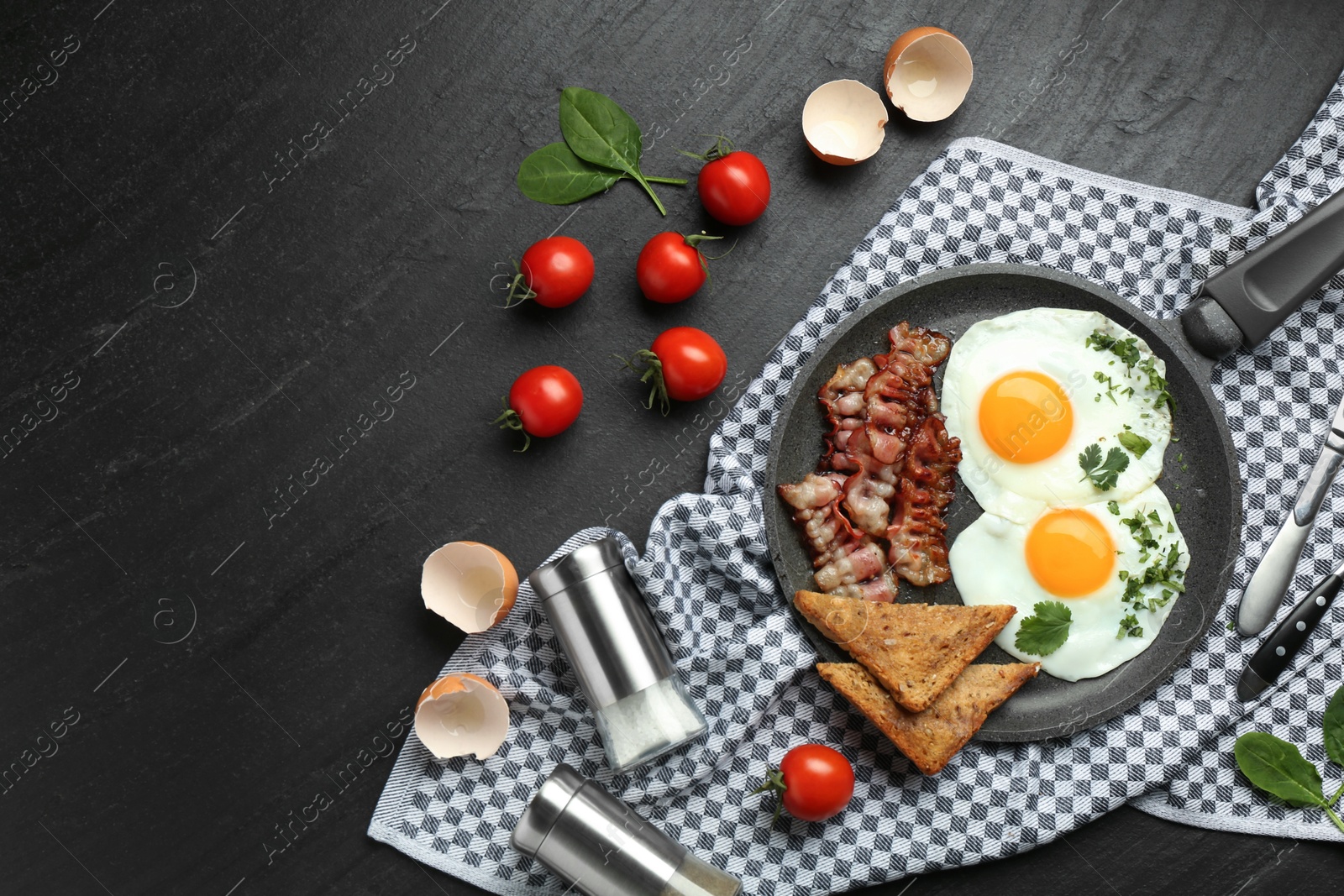 Photo of Tasty fried eggs, bacon and pieces of toast served on black table, flat lay. Space for text