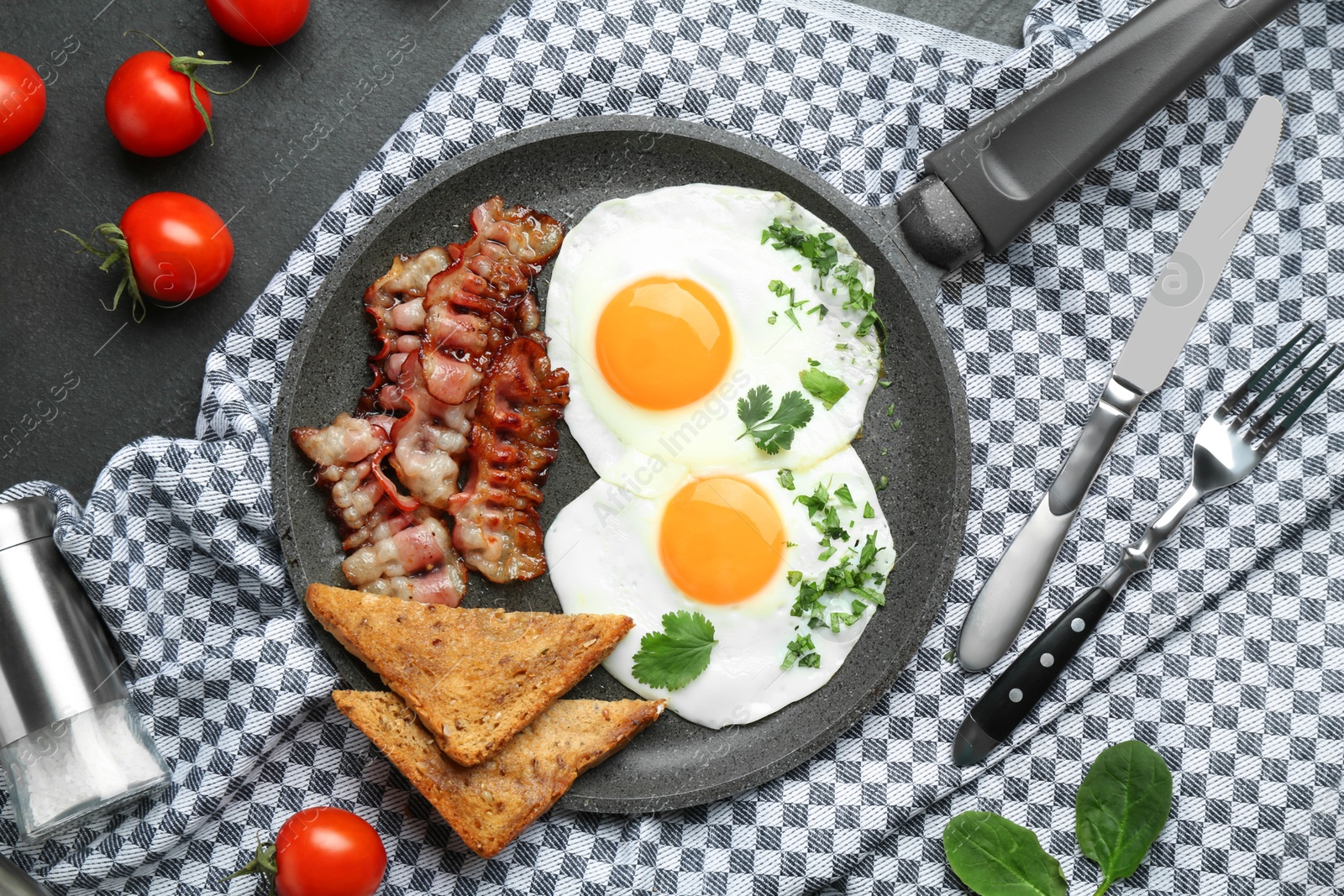 Photo of Tasty fried eggs, bacon and pieces of toast served on black table, flat lay