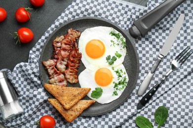 Photo of Tasty fried eggs, bacon and pieces of toast served on black table, flat lay