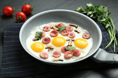 Photo of Tasty fried eggs with cut sausages and mushrooms served on black table, closeup