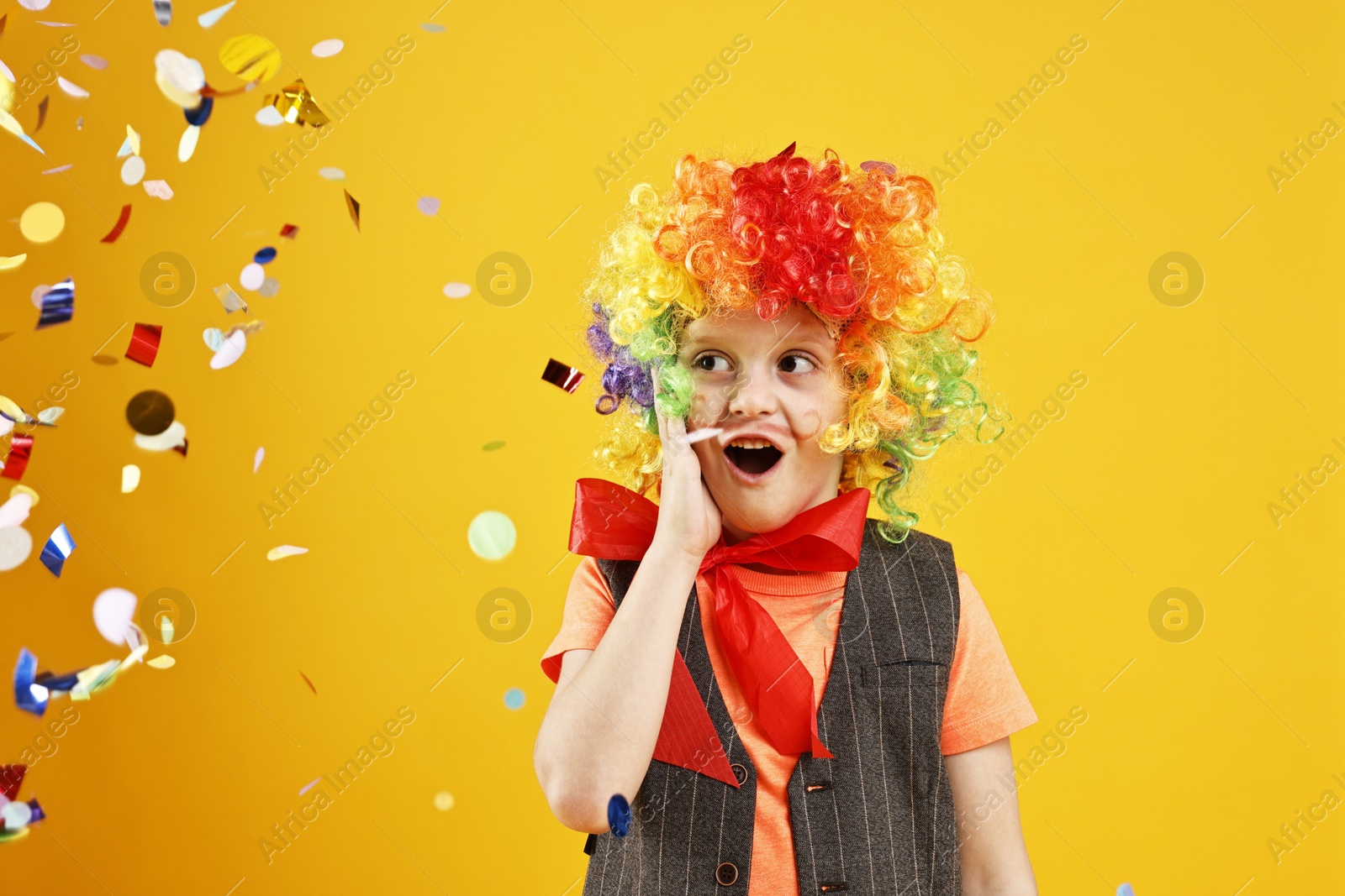 Photo of Surprised boy dressed like clown and flying confetti on orange background. Surprise party