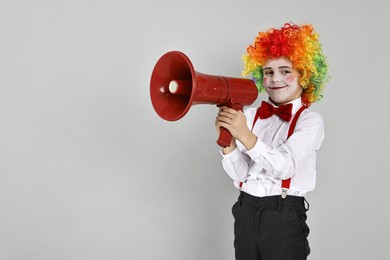 Little boy dressed like clown with megaphone on grey background, space for text. Surprise party