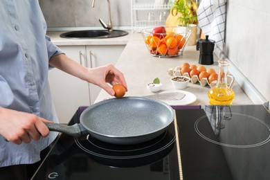 Photo of Woman breaking egg into frying pan in kitchen, closeup