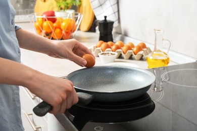 Photo of Woman breaking egg into frying pan in kitchen, closeup