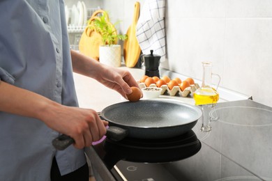 Photo of Woman breaking egg into frying pan in kitchen, closeup