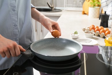 Photo of Woman breaking egg into frying pan in kitchen, closeup