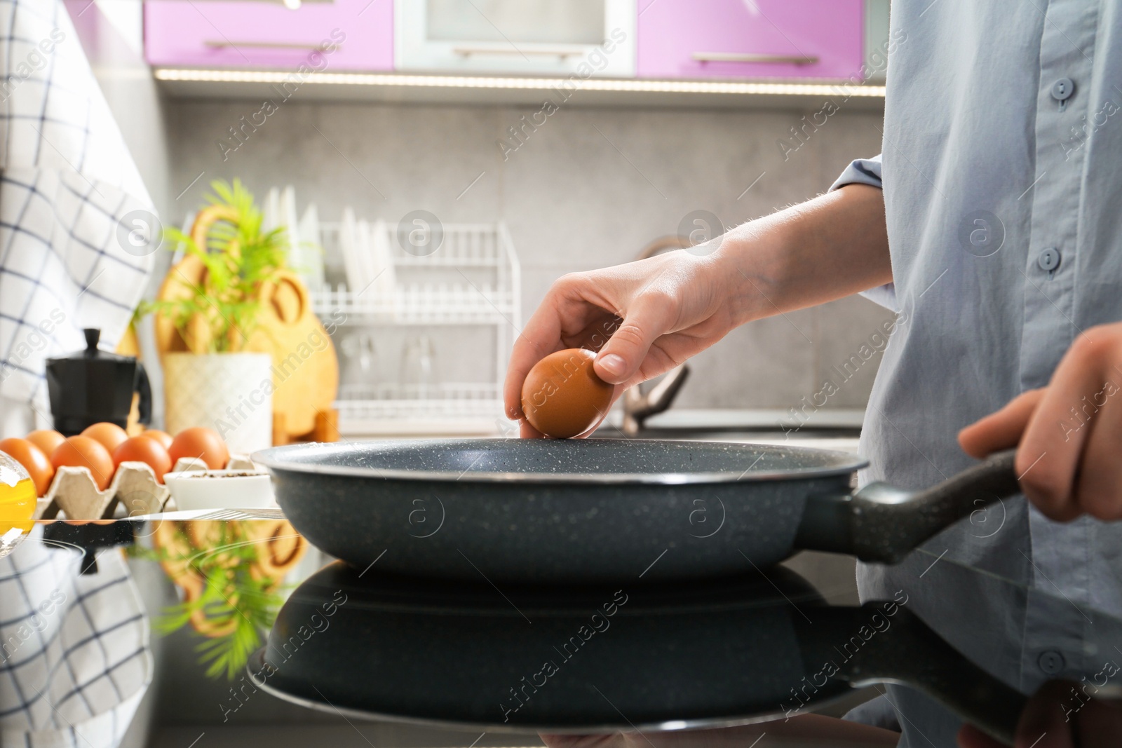 Photo of Woman breaking egg into frying pan in kitchen, closeup