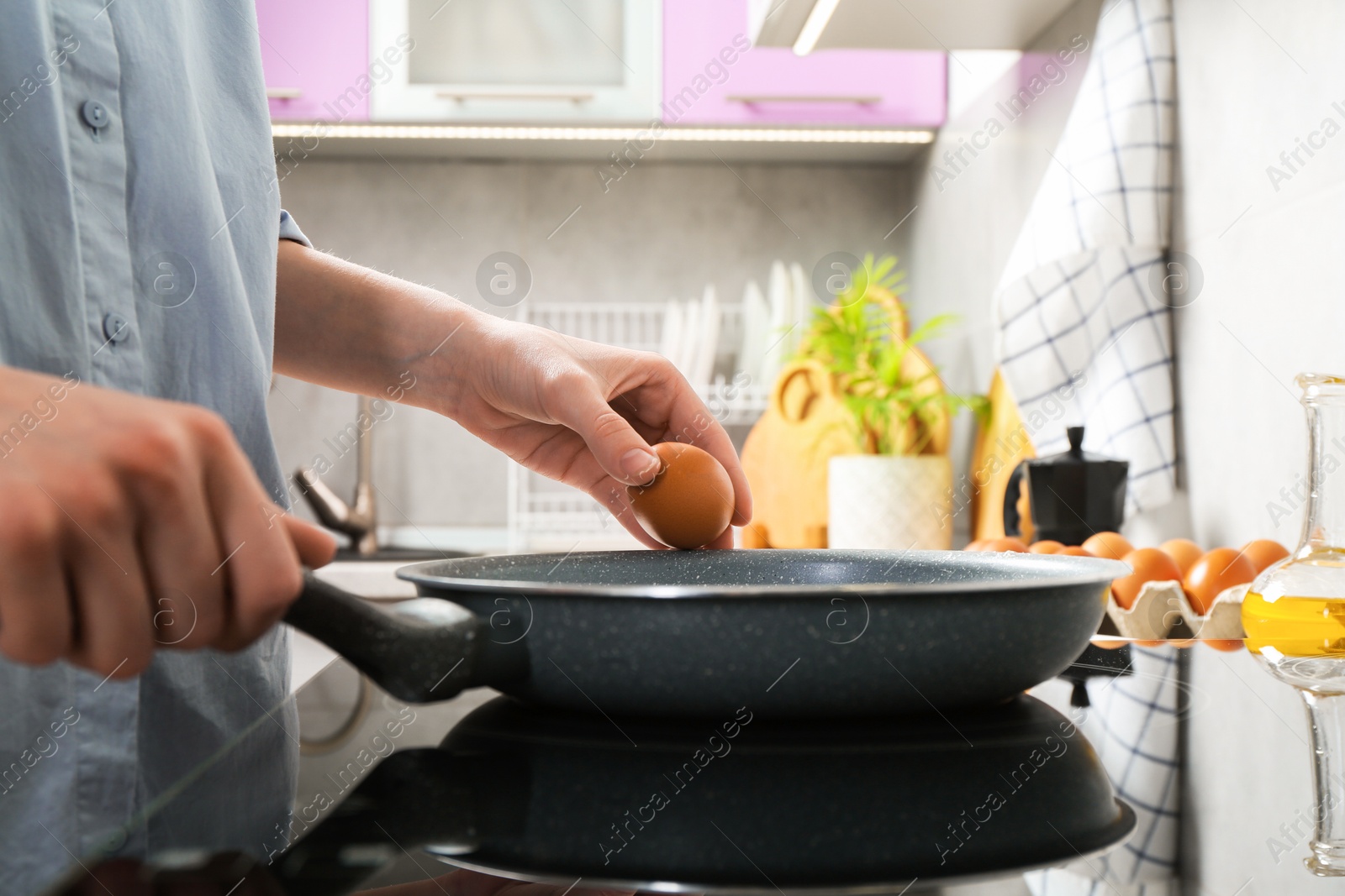 Photo of Woman breaking egg into frying pan in kitchen, closeup