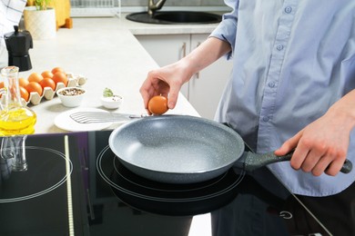 Photo of Woman breaking egg into frying pan in kitchen, closeup