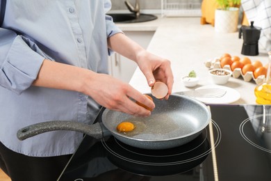 Photo of Woman breaking egg into frying pan in kitchen, closeup