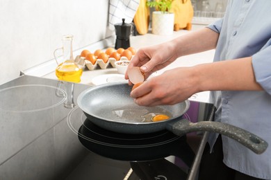 Photo of Woman breaking egg into frying pan in kitchen, closeup