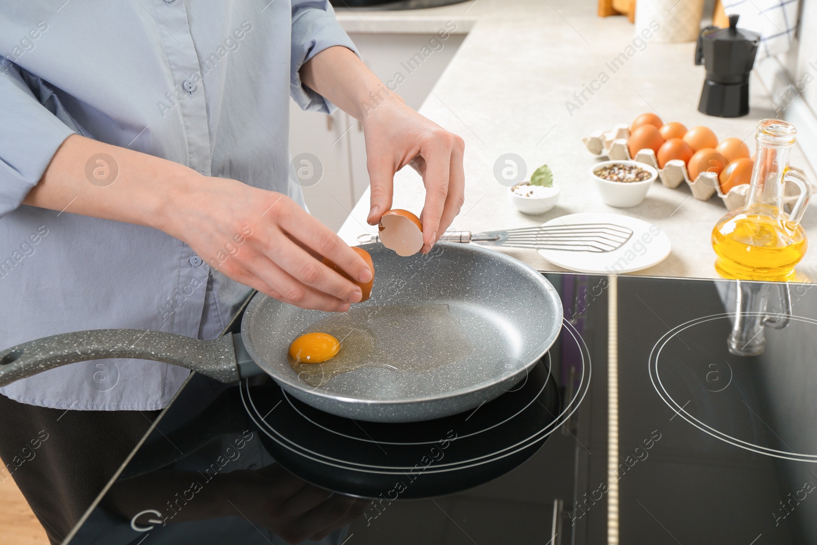 Photo of Woman breaking egg into frying pan in kitchen, closeup