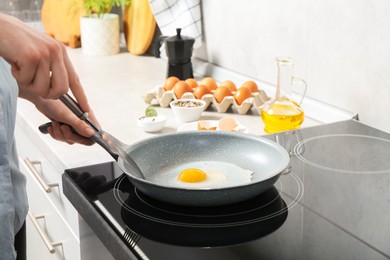 Photo of Woman with slotted turner cooking egg in frying pan on cooktop indoors, closeup